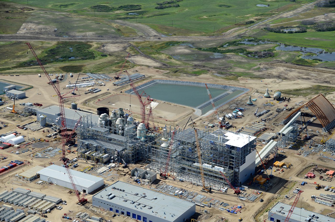 Aerial view of a large potash processing plant under construction, with numerous cranes and a process pond.