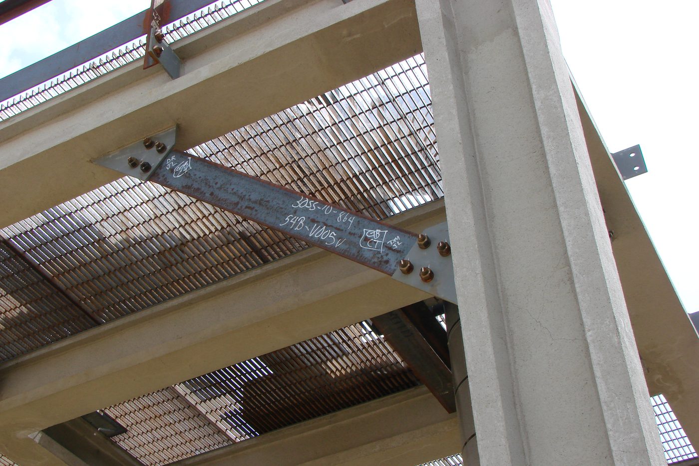 Bolted steel bracing member connected to a concrete column, with steel grating floors above.