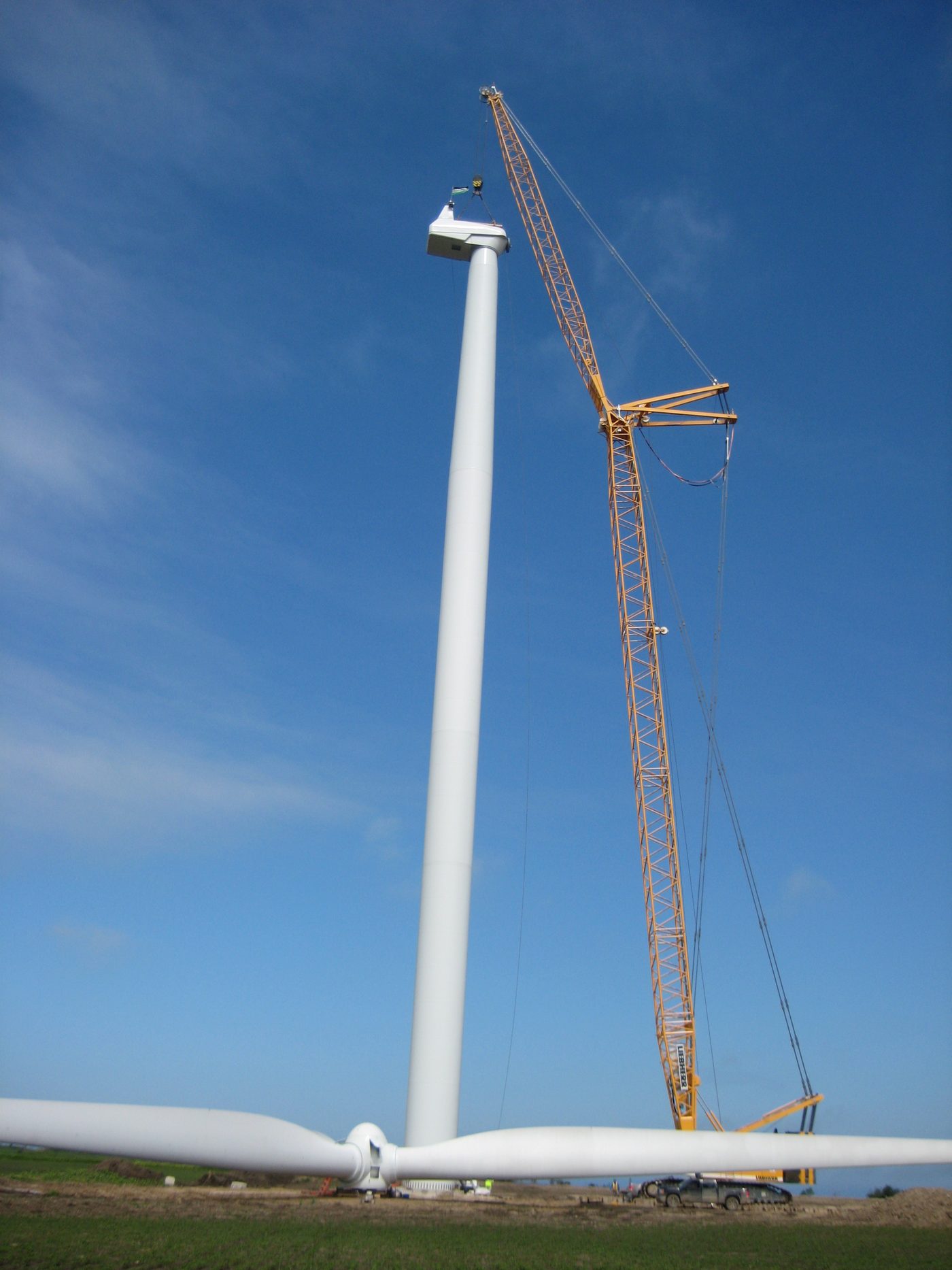 Wind turbine tower section being lifted into position by a crawler crane during installation.