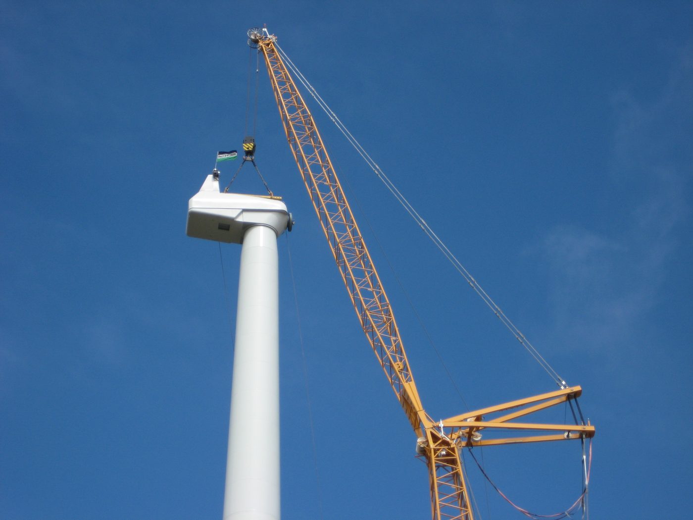 Crane lifting a wind turbine nacelle into position beside the completed tower.